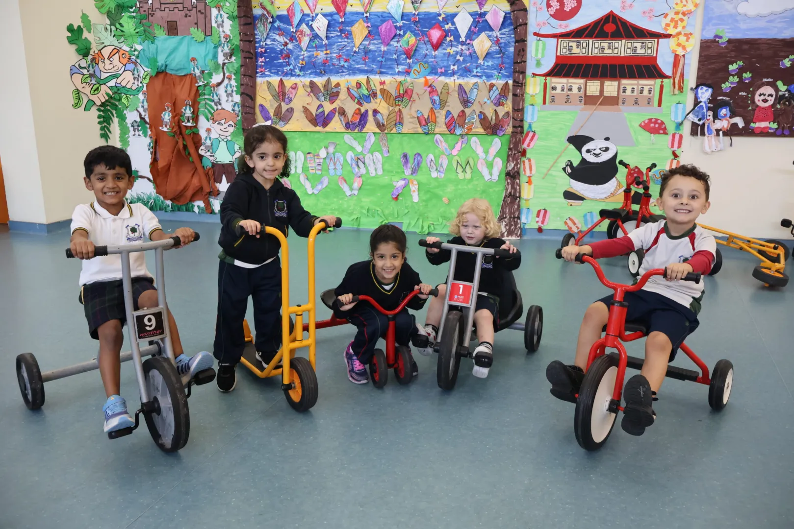 Students using tricycles and outdoor equipment to develop coordination and physical health on the school playground.